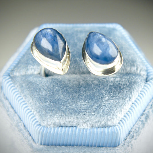 A pair of silver stud ringwith teardrop-shaped blue gemstones, displayed on a light blue velvet ring box.