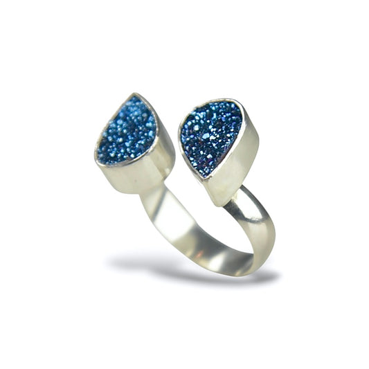 A silver ring featuring two teardrop-shaped blue glitter druzy stones set in a polished silver band, shown on a white background.