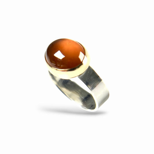 A silver ring featuring a round, polished amber-brown cabochon gemstone in a bezel setting, shown against a plain white background.
