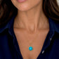 A close-up of a woman wearing a delicate gold chain necklace with a round turquoise pendant, styled with a dark navy blue collared shirt.