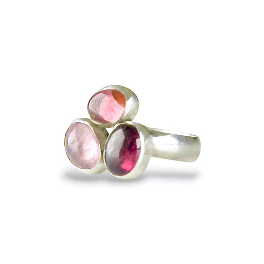 A silver ring featuring three oval-cut pink gemstones in a clustered setting, photographed on a clean white background.