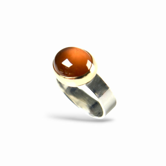 A silver ring featuring a round, polished amber-brown cabochon gemstone in a bezel setting, shown against a plain white background.